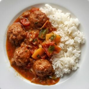 Création d'une photo pesant MAXIMUM 300ko d'un plat vu du haut dressé dans une assiette du plat plusieurs petites boulette de viande avec une sauce tomate aux légumes et riz de façon réaliste